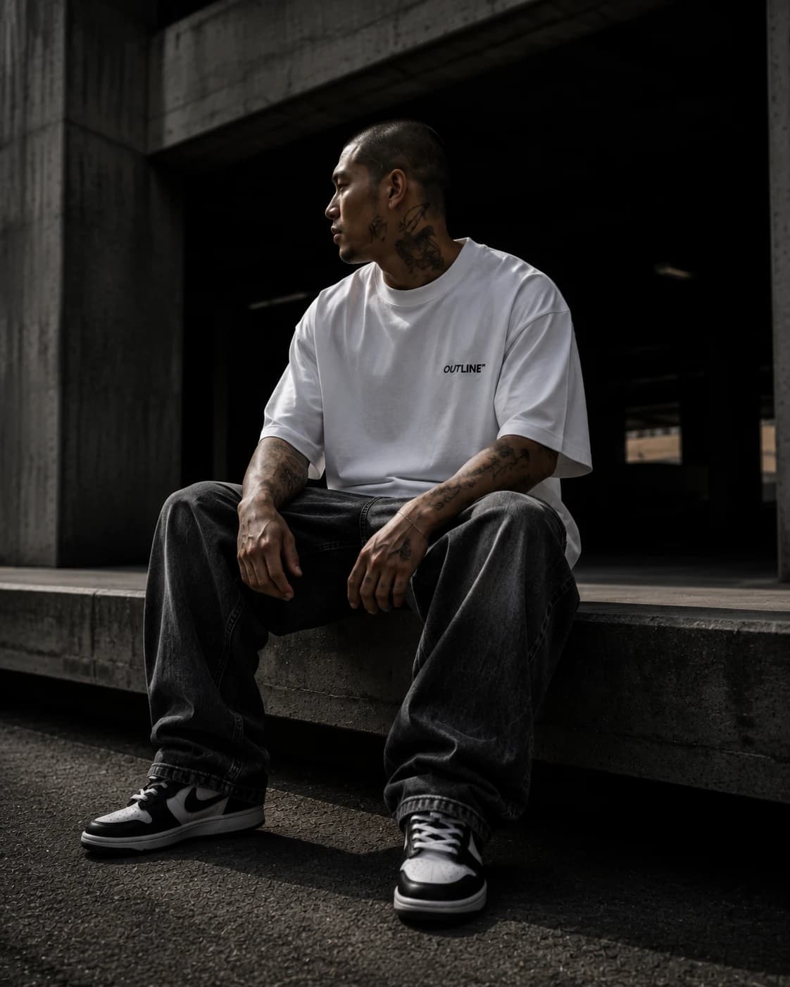 Model seated on a concrete ledge in white OUTLINE tee